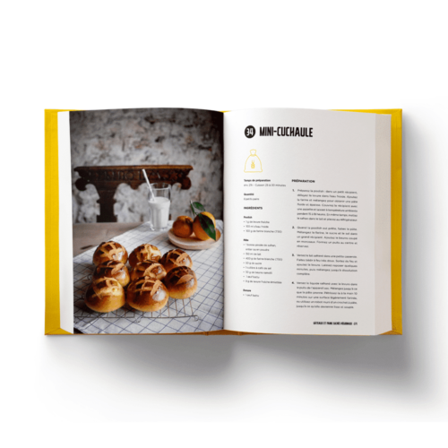 Livre ouvert Pains maison en français 42 recettes Helvetiq affichant une recette de mini-cuchaule sur une table avec des images du pain et un fond de cuisine rustique.